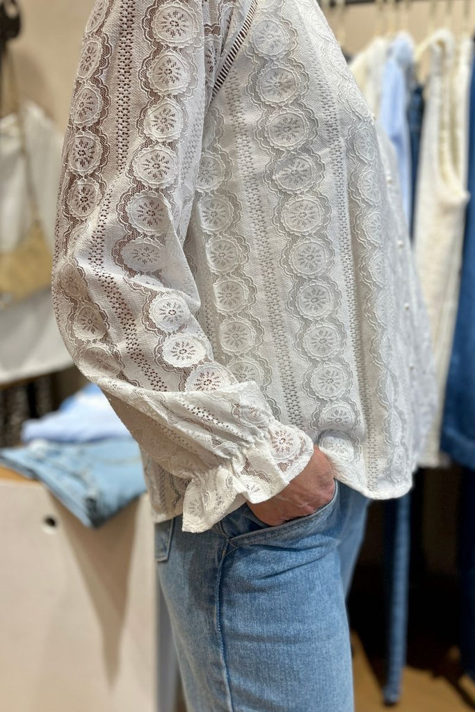 Blouse Giulia, couleur écru, manches longues resserrées sur le bas, matière broderie, encolure V, patte de boutonnage sur le devant