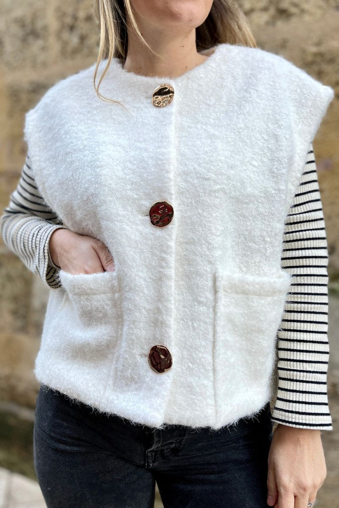 Gilet Amande, couleur écru, encolure ronde, boutons dorés fantaisies, sans manches, 2 poches plaquées sur le devnant